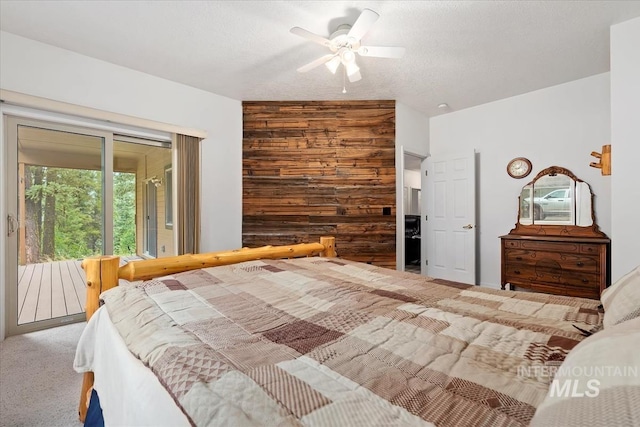 bedroom with wood walls, carpet, access to exterior, ceiling fan, and a textured ceiling