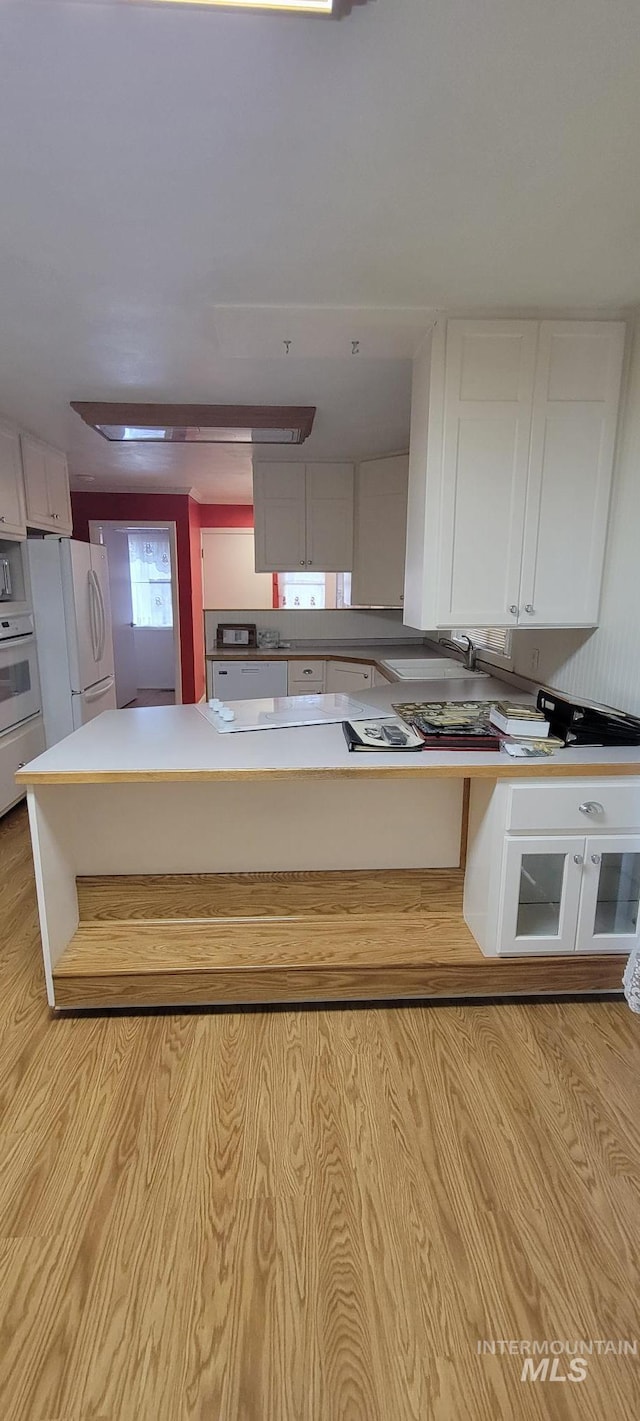 kitchen featuring white cabinets, light countertops, white appliances, light wood-style floors, and a peninsula