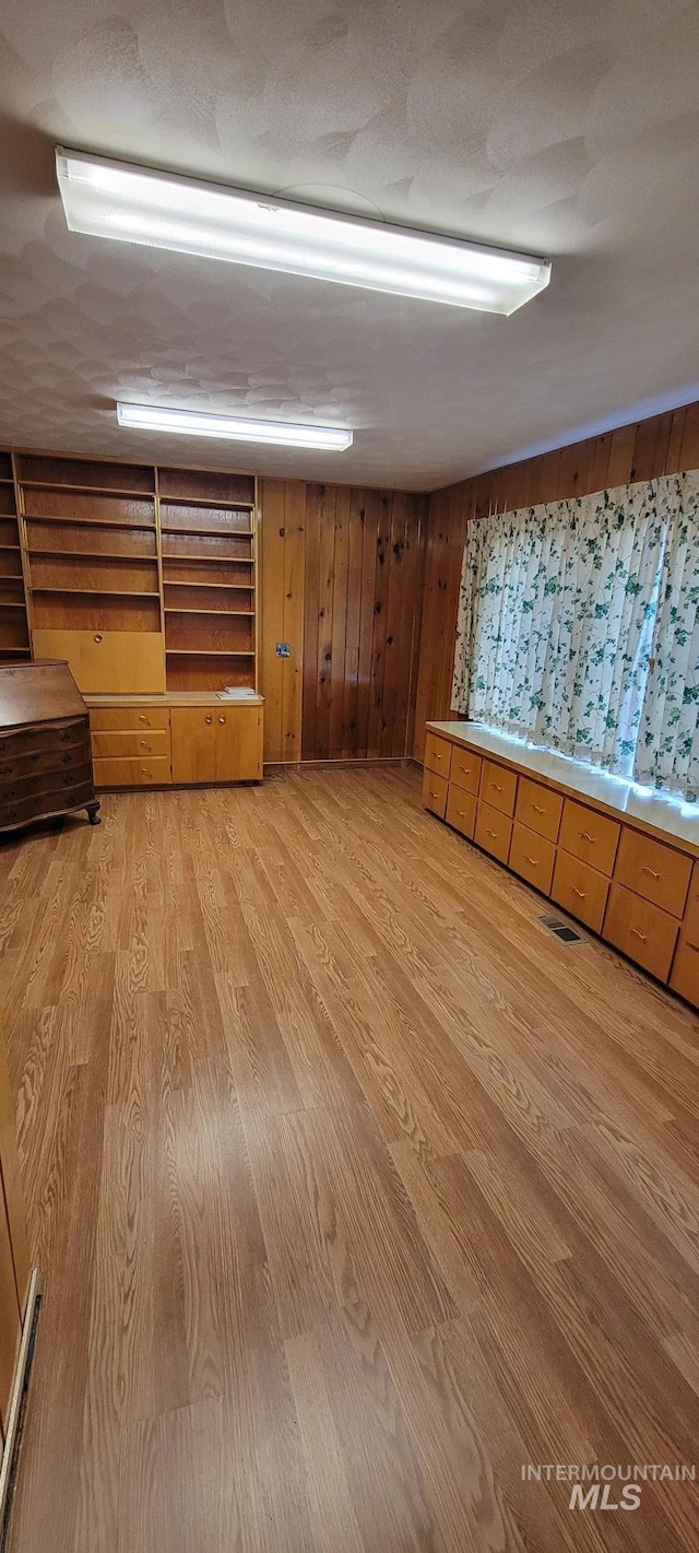 below grade area with a baseboard heating unit, visible vents, wood walls, and light wood-style floors