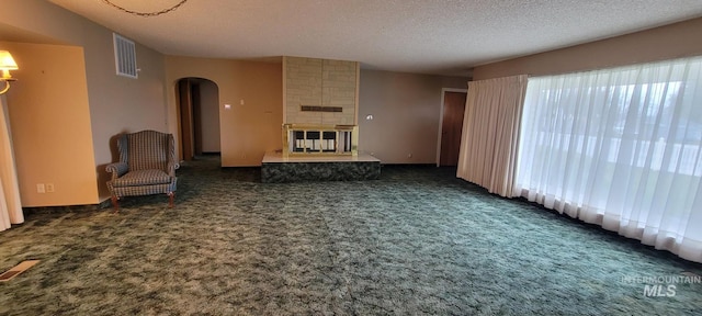 unfurnished living room with arched walkways, a textured ceiling, visible vents, carpet, and a fireplace