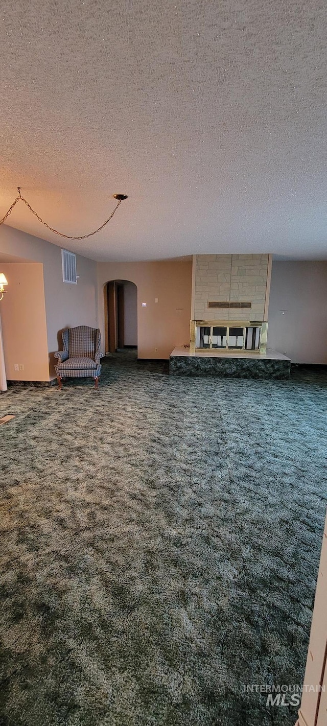 unfurnished living room with arched walkways, carpet flooring, and a textured ceiling