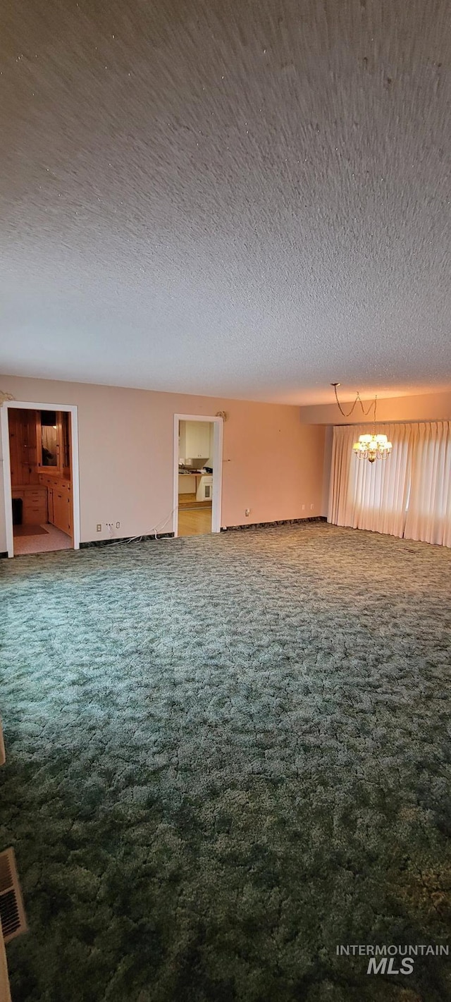 unfurnished living room featuring carpet floors, a textured ceiling, visible vents, and an inviting chandelier
