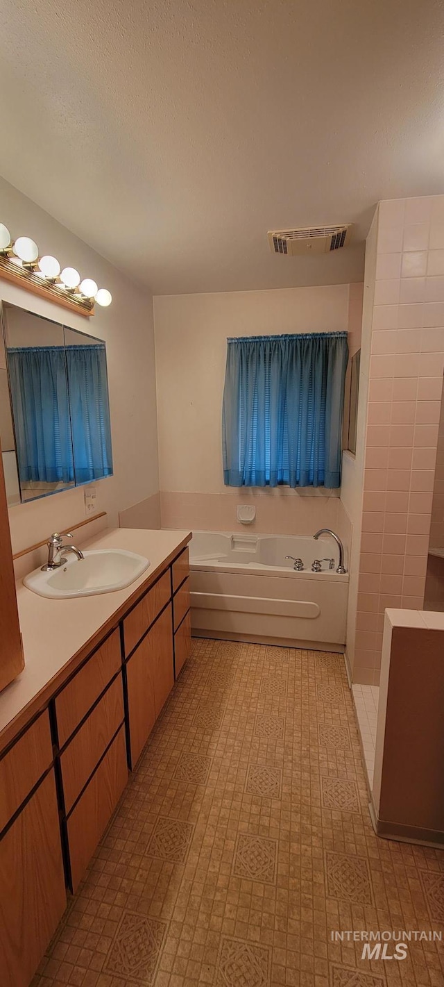 bathroom with a bath, visible vents, a textured ceiling, and vanity