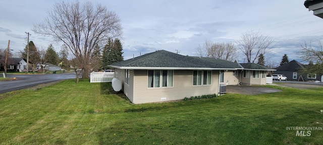 view of side of home featuring roof with shingles and a yard