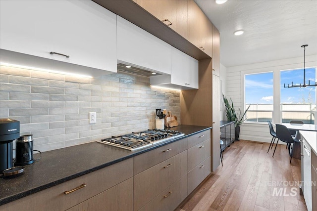 kitchen with stainless steel gas cooktop, custom exhaust hood, hanging light fixtures, light hardwood / wood-style floors, and decorative backsplash