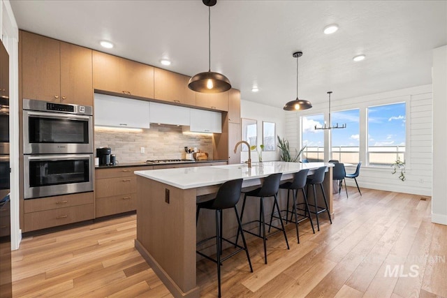 kitchen with a wealth of natural light, decorative light fixtures, backsplash, light hardwood / wood-style floors, and stainless steel appliances