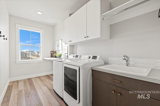 clothes washing area with cabinets, washer and dryer, sink, and light wood-type flooring