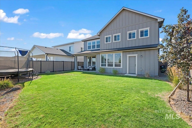 back of house with a trampoline and a lawn