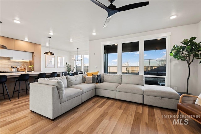 living room with ceiling fan with notable chandelier, a wealth of natural light, and light hardwood / wood-style flooring