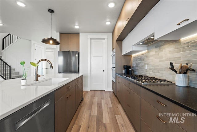 kitchen with sink, white cabinetry, hanging light fixtures, appliances with stainless steel finishes, and light hardwood / wood-style floors