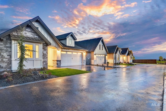 modern farmhouse with board and batten siding, fence, driveway, stone siding, and an attached garage