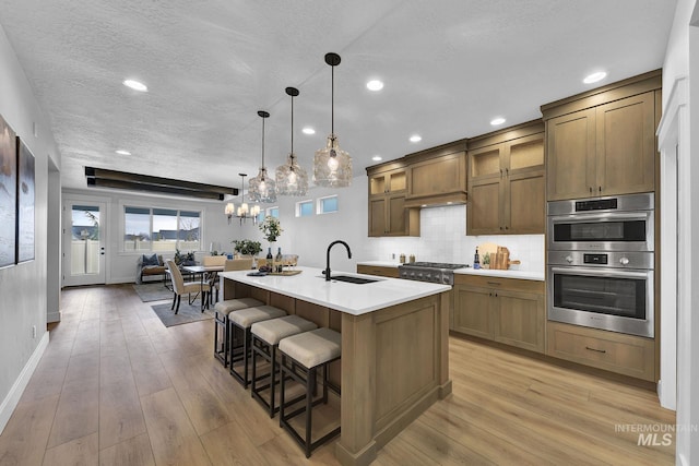 kitchen featuring light wood-style flooring, a sink, backsplash, appliances with stainless steel finishes, and light countertops