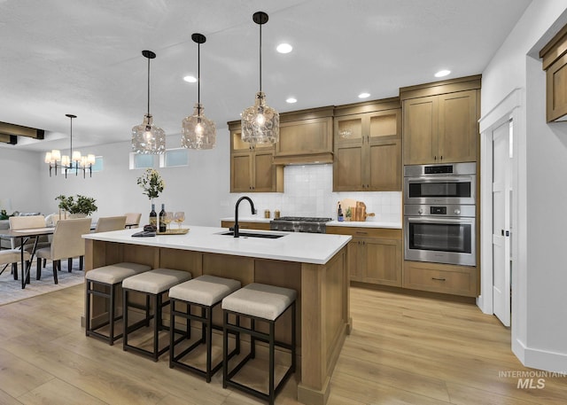 kitchen featuring light wood-type flooring, decorative backsplash, a kitchen breakfast bar, stainless steel appliances, and a sink