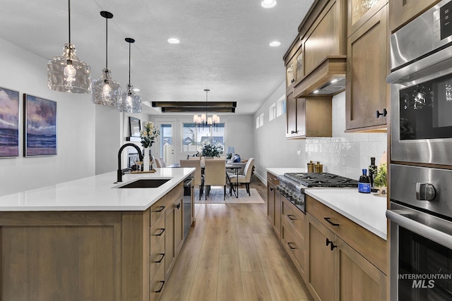 kitchen with light wood finished floors, a sink, backsplash, stainless steel appliances, and light countertops