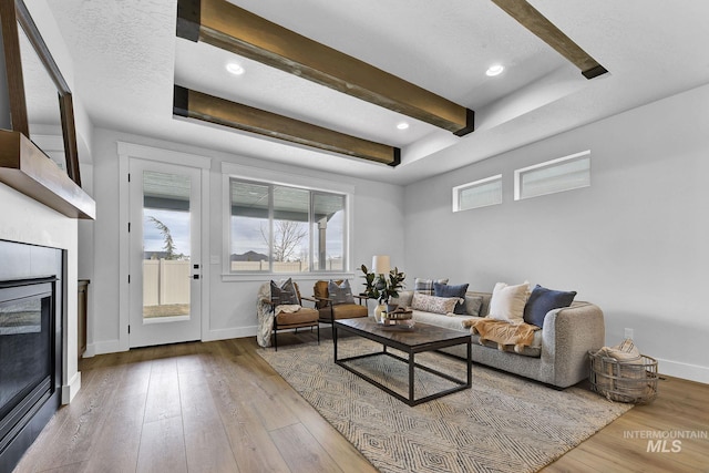 living room with a glass covered fireplace, hardwood / wood-style flooring, beamed ceiling, and baseboards