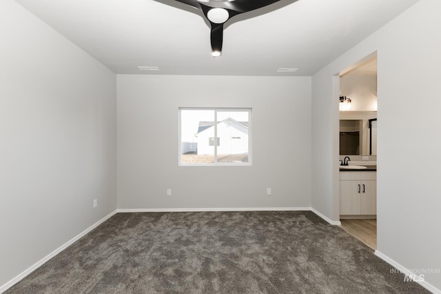 empty room featuring carpet floors, a sink, and baseboards