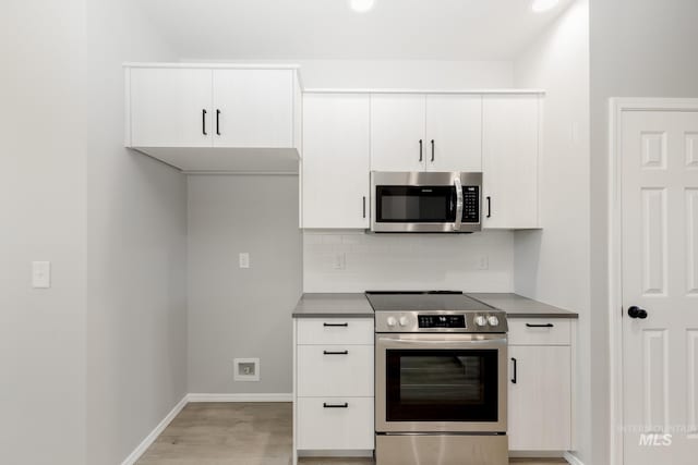 kitchen with light wood-style flooring, stainless steel appliances, white cabinetry, tasteful backsplash, and dark countertops