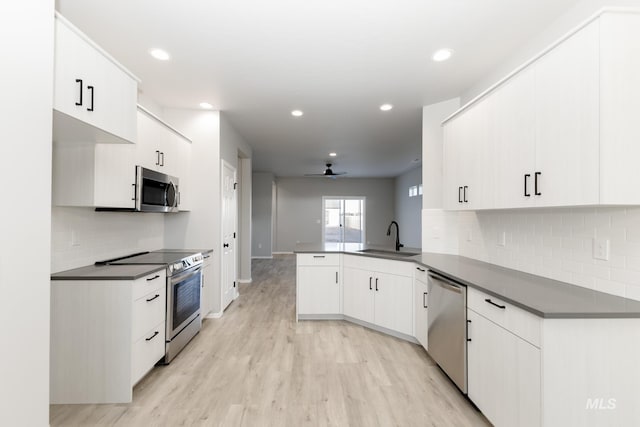 kitchen with dark countertops, appliances with stainless steel finishes, a peninsula, light wood-style floors, and a sink