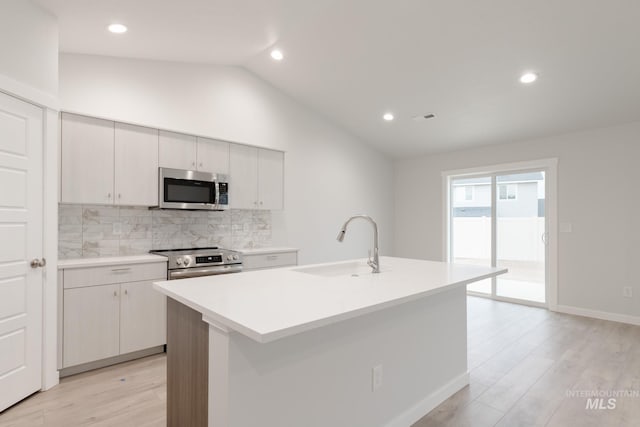 kitchen with a sink, lofted ceiling, stainless steel appliances, light wood finished floors, and backsplash
