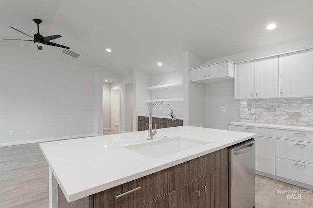 kitchen featuring a sink, an island with sink, white cabinetry, decorative backsplash, and light wood-style floors