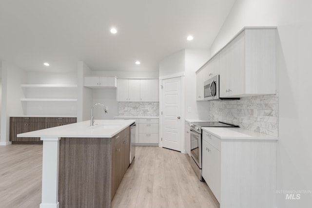 kitchen with a sink, white cabinets, light wood-type flooring, appliances with stainless steel finishes, and decorative backsplash