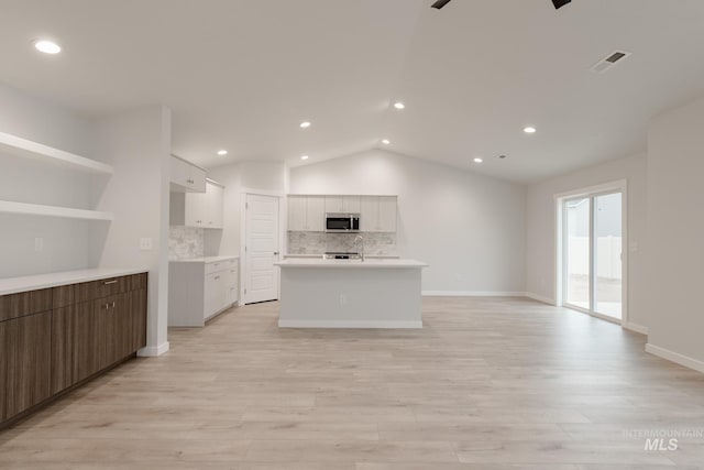 kitchen featuring stainless steel microwave, lofted ceiling, tasteful backsplash, light wood finished floors, and white cabinetry