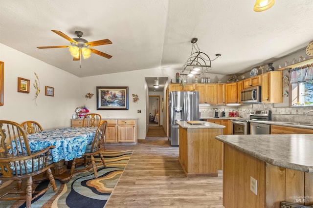 kitchen with a ceiling fan, appliances with stainless steel finishes, a center island, vaulted ceiling, and light wood-style floors