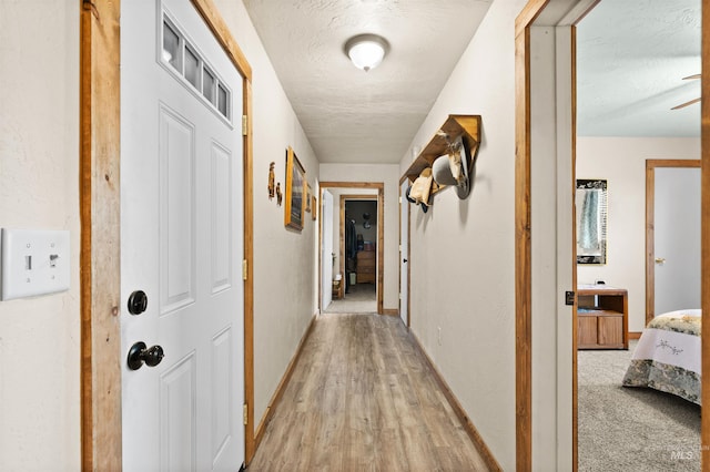 hall featuring baseboards, a textured ceiling, and light wood-style flooring