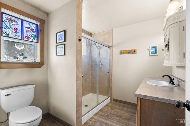 bathroom featuring vanity, toilet, baseboards, wood finished floors, and a stall shower