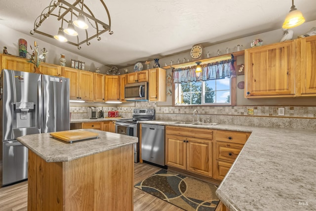 kitchen with decorative light fixtures, appliances with stainless steel finishes, a center island, a sink, and light wood finished floors