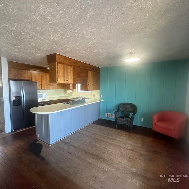 kitchen with kitchen peninsula, a textured ceiling, dark wood-type flooring, stainless steel refrigerator with ice dispenser, and sink