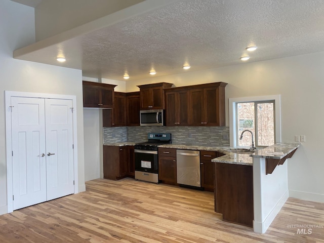 2504 E Hidden Creek St, Nampa, ID 83687 - kitchen with stainless steel appliances, a peninsula, light wood-style floors, a textured ceiling, and light stone counters