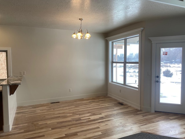 2504 E Hidden Creek St, Nampa, ID 83687 - unfurnished dining area with light wood-style floors, a chandelier, a textured ceiling, and baseboards