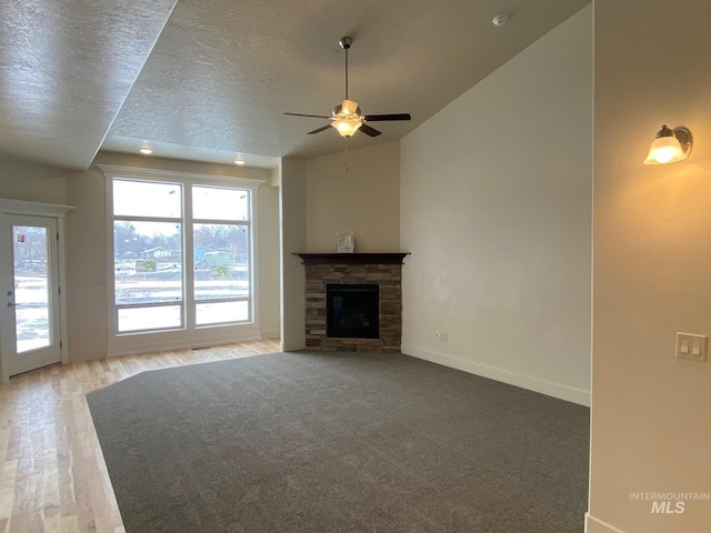 2504 E Hidden Creek St, Nampa, ID 83687 - unfurnished living room with baseboards, a ceiling fan, a stone fireplace, a textured ceiling, and wood finished floors
