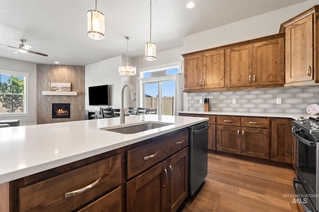 kitchen featuring a sink, stainless steel appliances, light countertops, backsplash, and a fireplace