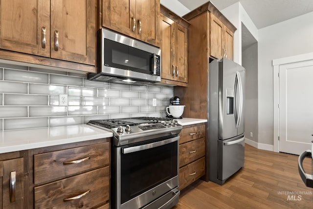 kitchen featuring stainless steel appliances, wood finished floors, decorative backsplash, baseboards, and light countertops
