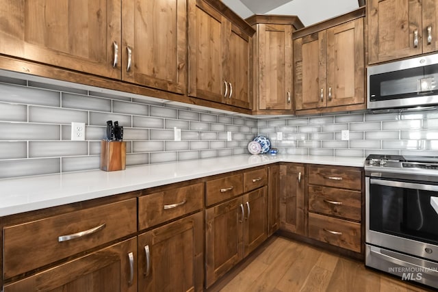 kitchen with appliances with stainless steel finishes, light wood-type flooring, tasteful backsplash, and light countertops