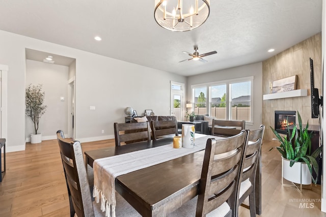 dining area featuring a fireplace, ceiling fan, recessed lighting, light wood-type flooring, and a chandelier