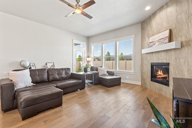 living room with a ceiling fan, light wood-style flooring, a tile fireplace, baseboards, and recessed lighting