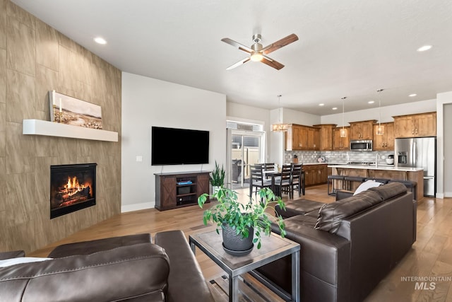 living area featuring light wood-style floors, baseboards, ceiling fan, recessed lighting, and a fireplace