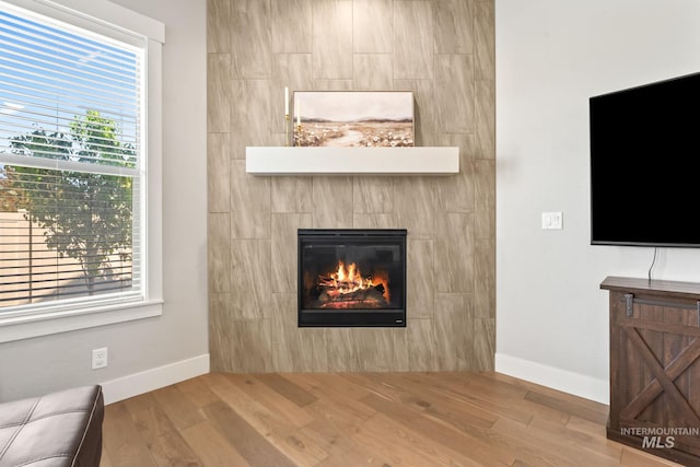 unfurnished living room with wood finished floors, a fireplace, baseboards, and healthy amount of natural light
