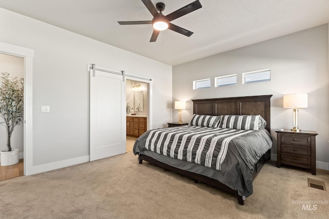 bedroom featuring a barn door, light colored carpet, baseboards, ensuite bath, and ceiling fan