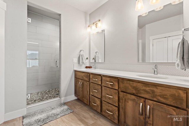 bathroom with a shower stall, double vanity, decorative backsplash, and baseboards