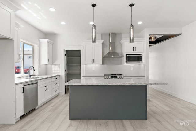 kitchen with white cabinets, light stone counters, wall chimney range hood, and appliances with stainless steel finishes