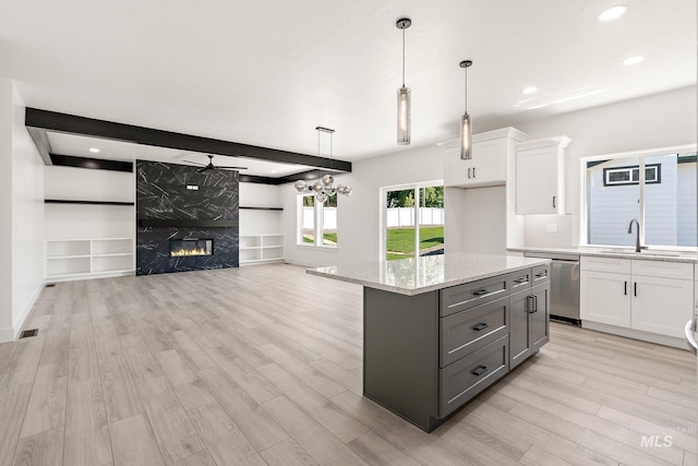 kitchen featuring stainless steel dishwasher, a kitchen island, sink, decorative light fixtures, and white cabinetry