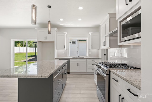 kitchen featuring appliances with stainless steel finishes, light stone counters, pendant lighting, white cabinetry, and a kitchen island