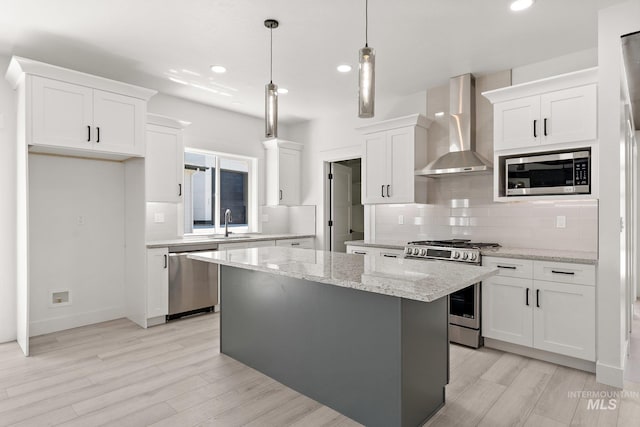 kitchen with a center island, wall chimney exhaust hood, hanging light fixtures, stainless steel appliances, and white cabinets