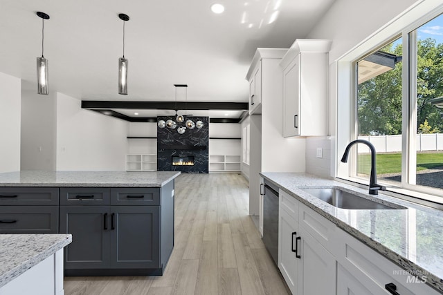 kitchen with sink, stainless steel dishwasher, a fireplace, light hardwood / wood-style floors, and white cabinetry