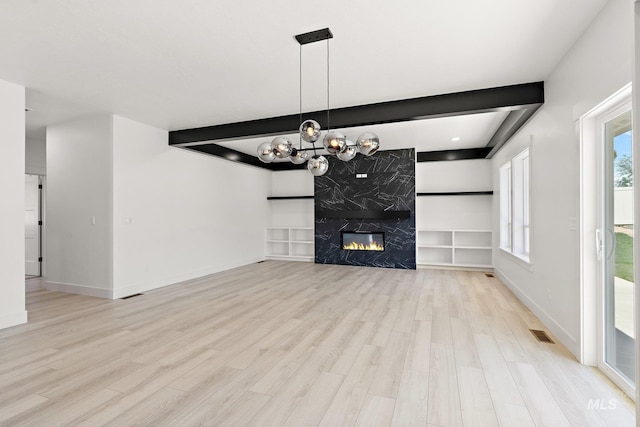 unfurnished living room featuring beamed ceiling, light hardwood / wood-style floors, a fireplace, and a chandelier