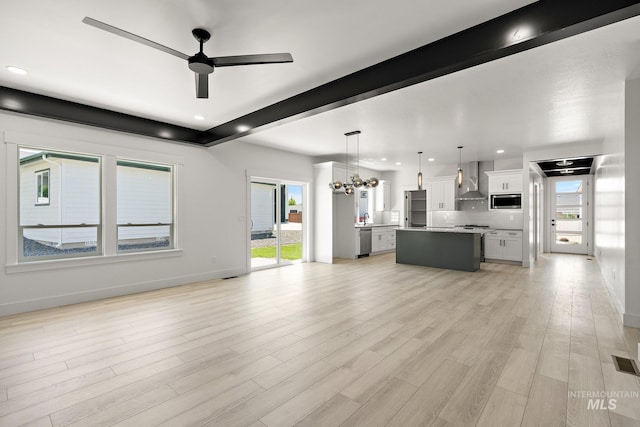 unfurnished living room featuring beamed ceiling, plenty of natural light, light wood-type flooring, and ceiling fan with notable chandelier